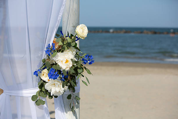 White and blue flowers decorate a wedding gazebo on a sandy beach overlooking the ocean