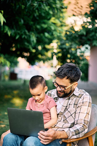 istock Son is sitting in father's lap in a backyard and typing on a laptop. 2222407380