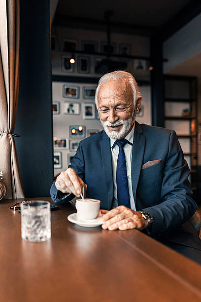 istock Senior Man in Suit Stirring Coffee in Cozy Cafe 2222414459