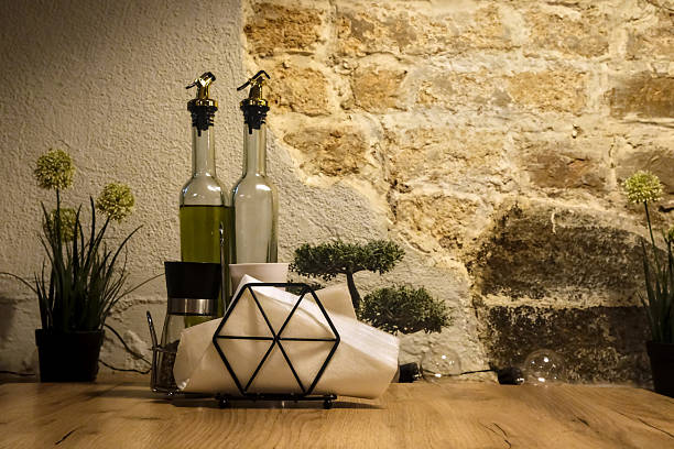 Rustic tabletop setting with olive oil bottles, napkins, and small plants against a stone wall, evoking a cozy Mediterranean ambiance.