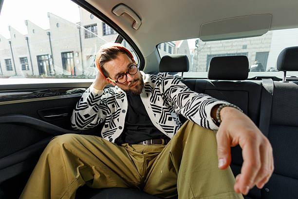 Casually dressed young man sitting relaxed in the backseat of a car in a playful and comfortable freestyle pose.