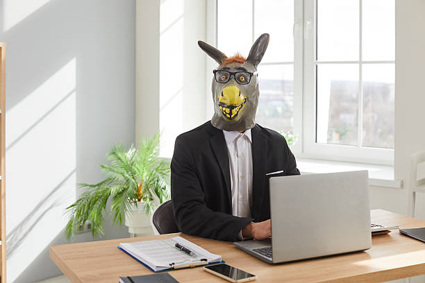 istock Businessman in donkey head mask using laptop computer in office 2222418736