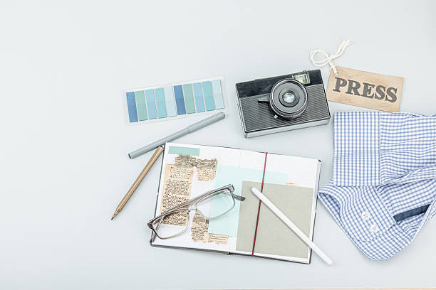 Flat lay of retro journalist essentials on blue background: camera, press badge, notebook, newspaper clippings, and stationery. OSINT and media storytelling theme, top view