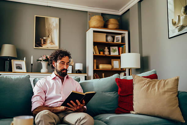 istock Man reading a book on the sofa in his living room 2222440668