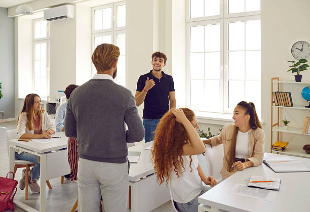 istock Bearded teacher communicates with student through desk against background of large bright window in modern classroom. 2222440957
