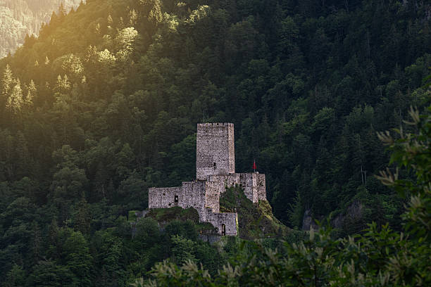 A medieval stone castle with a Turkish flag on top, set against a bright blue sky in a mountainous region.