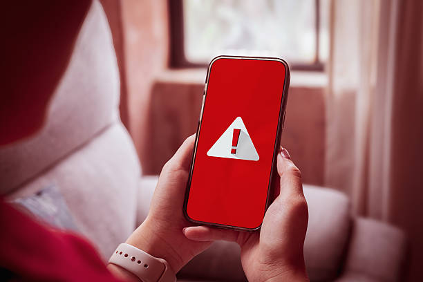istock Woman using smartphone showing red screen with warning triangle exclamation mark indicating system error. 2222441334