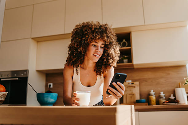 istock Smiling woman drinking milk and using her phone in a bright kitchen 2222444219