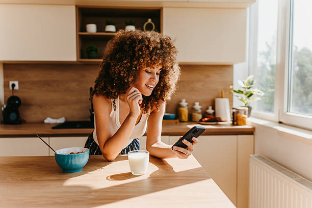 istock Young woman enjoying breakfast and checking her phone in a modern kitchen 2222444220