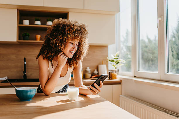 istock Smiling woman using smartphone and having breakfast in kitchen 2222444293