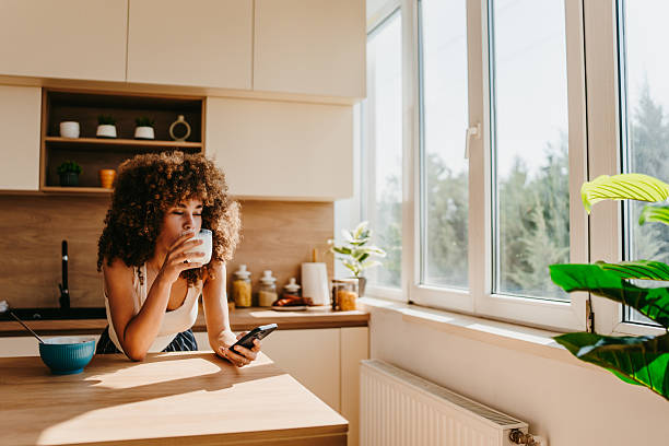 istock Young woman enjoying breakfast and checking her phone in a modern kitchen 2222444306