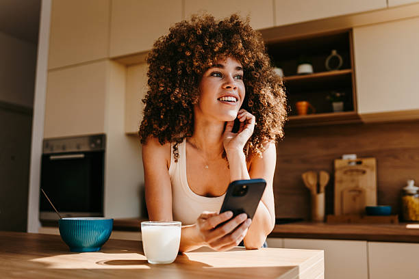 istock Young woman using smartphone and having breakfast in kitchen 2222444317