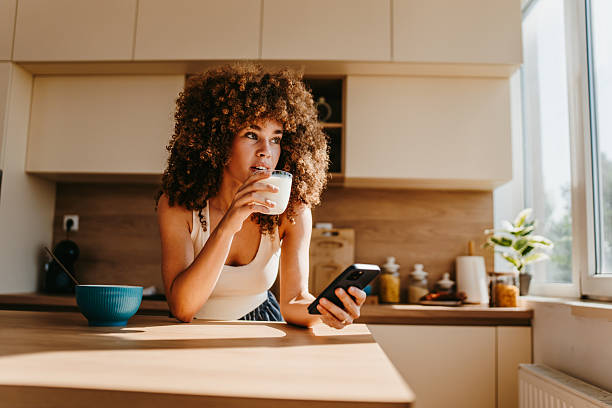istock Young woman drinking milk and using smartphone in kitchen during breakfast 2222444324