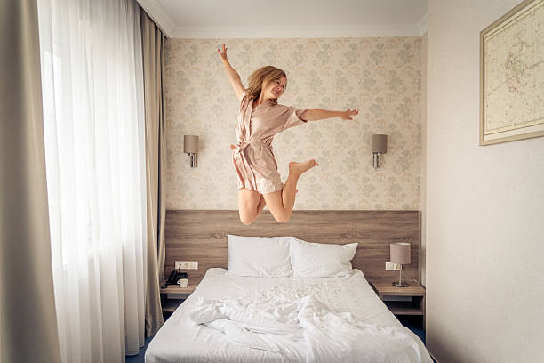 istock Woman having fun and jumping with bathrobe on bed in hotel room 2222448444