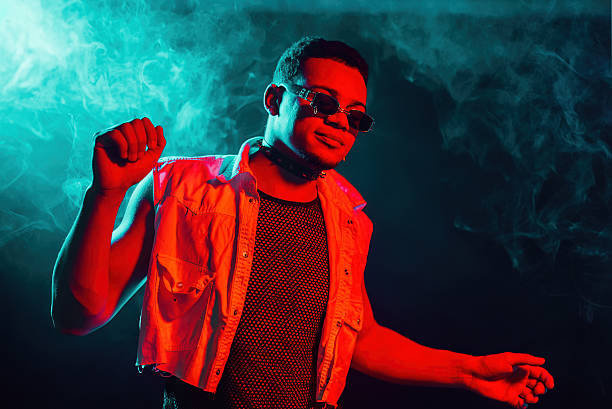 Stylish man dressed in transparent net dancing in neon light, smoke studio or in night club. Portrait of sexy guy with curly hair. Active energy, inspired dance. High quality photo