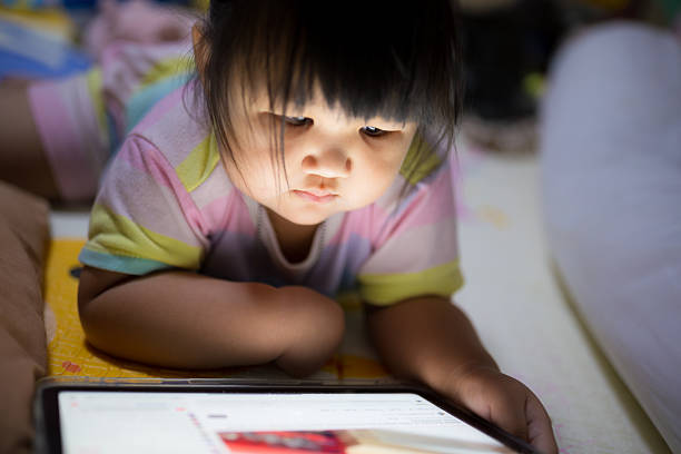 istock A little girl is lying down looking at a tablet screen,Asian girl lying on bed watching cartoons. Children using tablet in her free time. Children using touchpad for learning. Concept of young children and technology. 2222463708