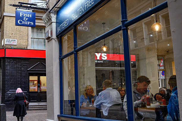 Two adult women sharing drinks and conversation inside a urban cafe, seen through the window with city reflections