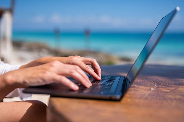 istock Close-up of a woman's hands typing on a laptop while sitting at a beach restaurant. 2222465828