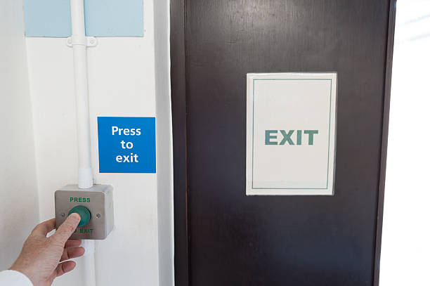 A dark corridor in a building with an illuminated exit sign, fire extinguisher, and bright natural light at the far end.