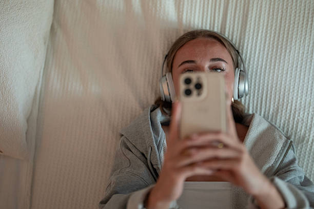 Person Lying in Bed Using Smartphone and Headphones for Relaxation