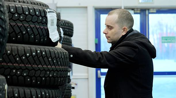 istock Professional mechanic selecting winter tires, comparing tread depth and performance characteristics in automotive service center showroom 2222476994
