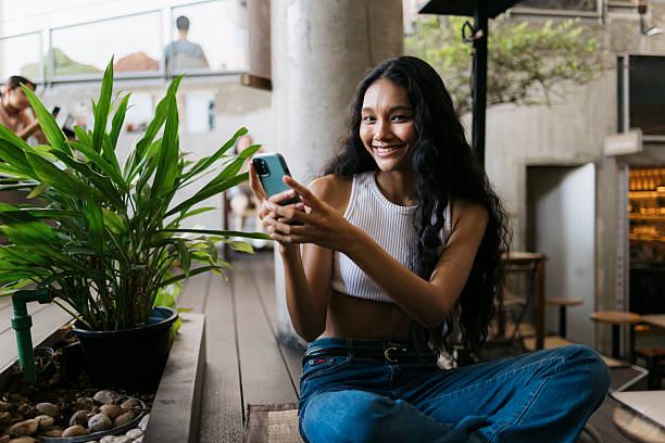 Smiling young woman using mobile sitting at cafe
