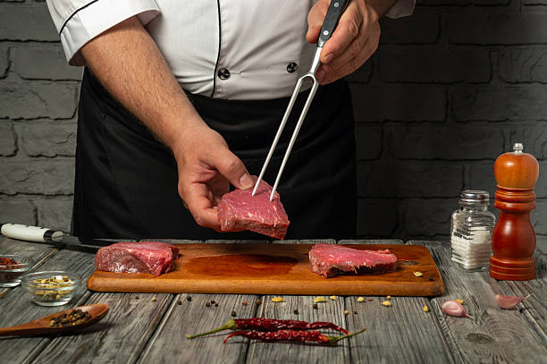 istock A chef is skillfully handling a piece of raw meat with a fork, surrounded by spices and ingredients on a wooden board in a rustic kitchen setting at night 2222482449