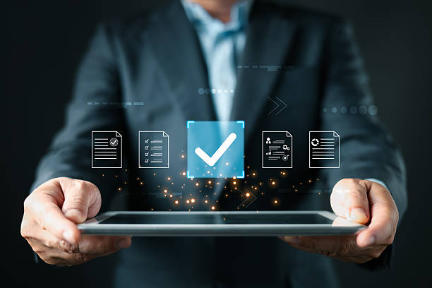 istock A business professional holds a tablet displaying floating document icons, a large checkmark symbolizing digital approve processes, focusing on business quality assurance and data management. 2222482480