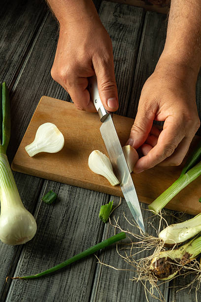 istock Hands skillfully cut fresh green onions on a wooden cutting board. The kitchen is filled with vibrant produce and earthy textures, enhancing the cooking atmosphere 2222482521