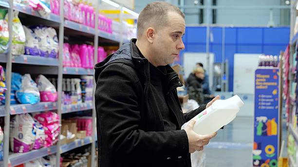 istock Focused shopper examining detergent bottle label, comparing cleaning products amid supermarket shelves stocked with household supplies 2222482608