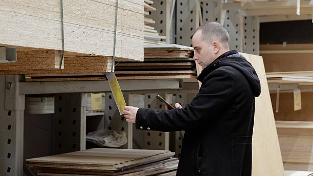 istock Carpenter browsing wooden boards in warehouse, scanning bar codes, comparing prices on smartphone while carefully examining lumber quality and specifications 2222483790