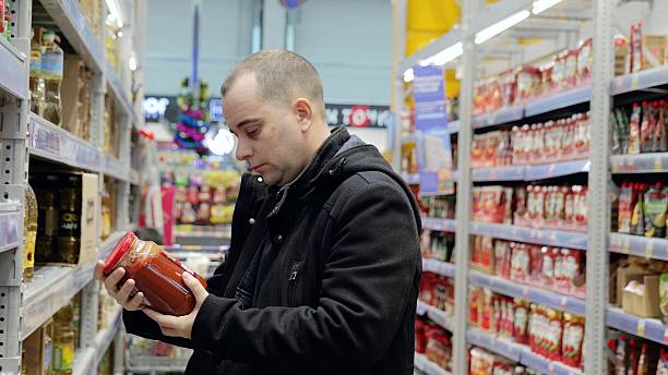 istock Male shopper selecting tomato sauce jar, examining product label, comparing brands while grocery shopping in supermarket aisle 2222485145