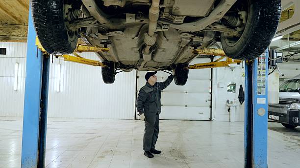 istock Skilled mechanic inspecting vehicle underside on hydraulic lift, checking mechanical components in modern automotive workshop repair environment 2222489820