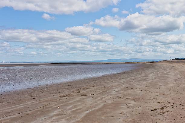 istock A wide, sandy beach stretches out under a sky filled with scattered clouds. 2222499577
