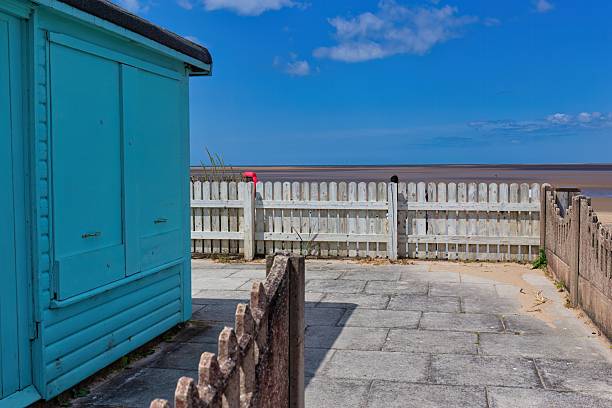 istock A quaint blue beach hut sits beside a white picket fence overlooking a serene beach and sky. 2222499735