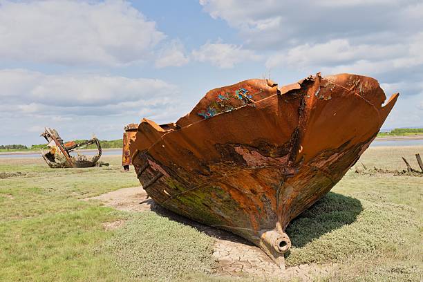 istock Rusting metal shipwreck  sit on grassy ground under a cloudy sky. 2222499828