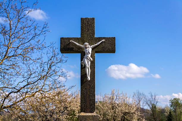 Beautiful Jesus Christ on crucifix, spring Easter budding tree flowers in background, cemetery on a sunny day, new life and religion concept