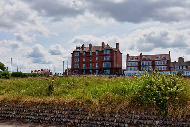 istock A grassy field leads to a brick building complex under a cloudy sky. 2222501051