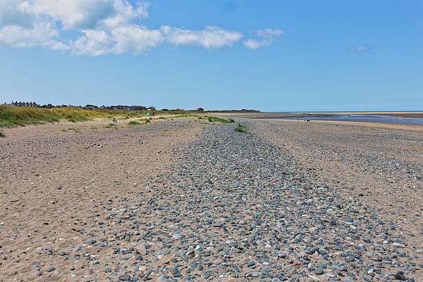 istock A scenic view of a beach featuring pebbles and sand under a bright, partly cloudy sky. 2222501061
