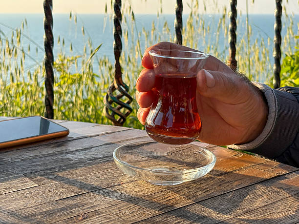 Turkish tea. Close-up of a male hand holding Turkish tea in an outdoor cafe or restaurant with sea background. Drinking Turkish tea