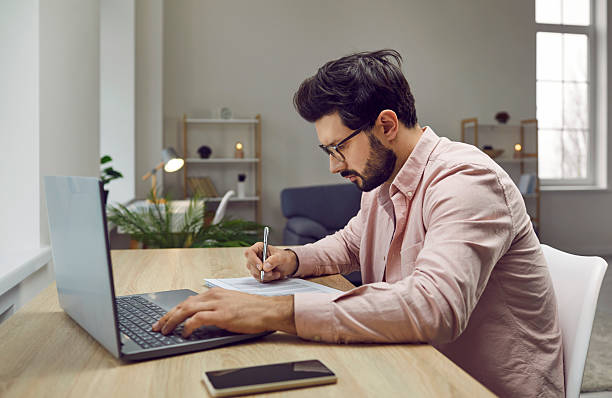 istock Young serious businessman working with laptop computer at home or at office and writing. 2222508286