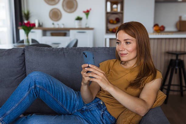 istock Smiling woman relaxing on sofa using smartphone at home 2222526689