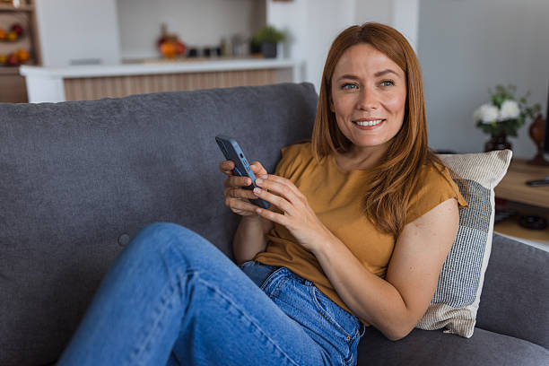 istock Smiling woman relaxing on sofa using smartphone at home 2222526695