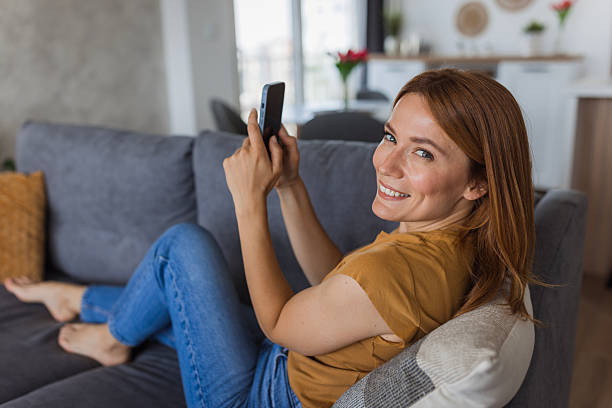 istock Smiling woman relaxing on sofa using smartphone at home 2222526713