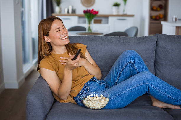 istock Woman laughing while watching tv and eating popcorn on sofa at home 2222526862