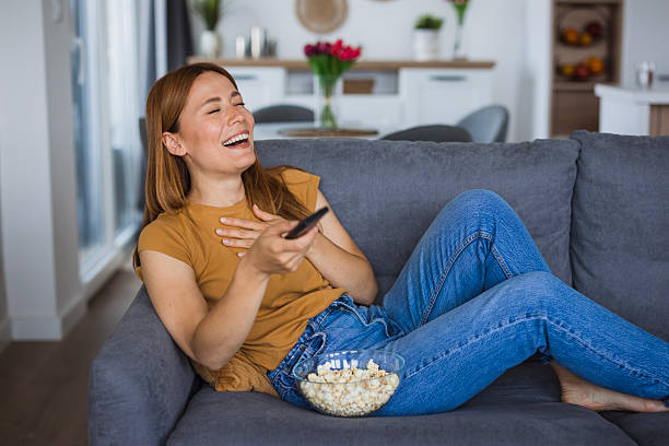 istock Woman laughing while watching tv and eating popcorn on sofa 2222526867