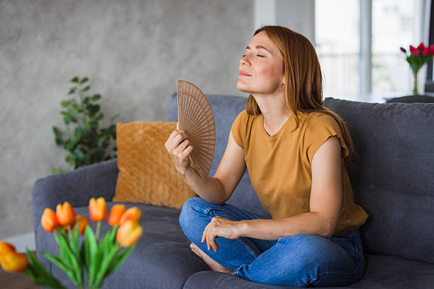 istock Woman cooling down on sofa with hand fan during hot summer day 2222526908