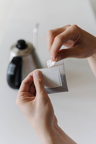 Man opening single-serve drip coffee bag, preparing to brew fresh cup of coffee with modern method at home in morning during breakfast, close-up.