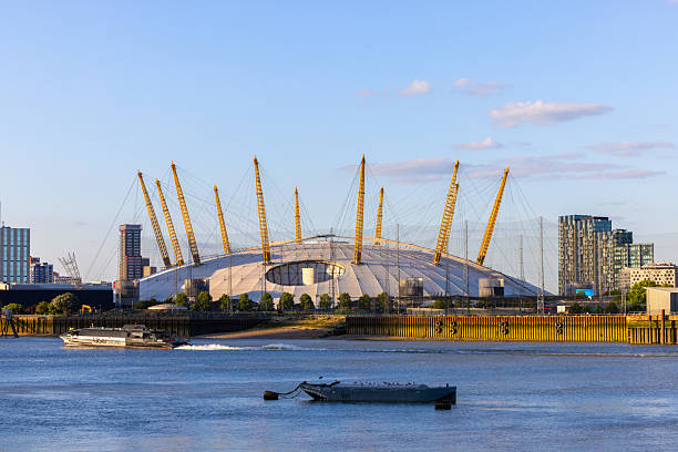 An Uber Boat by Thames Clippers travels along the River Thames at sunset, positioned between a small boat and the O2 Arena in North Greenwich, London. Captured from the Isle of Dogs on a summer evening.