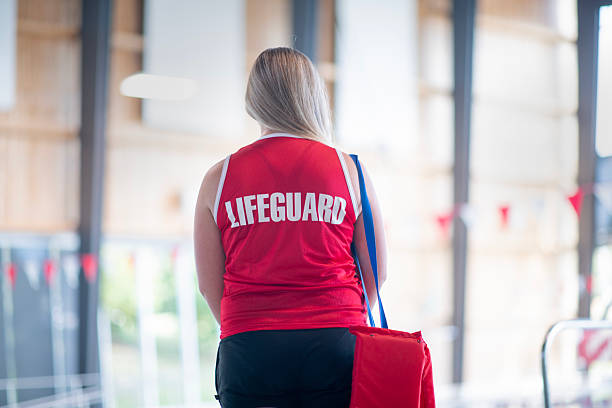 istock Lifeguard Standing by Indoor Pool in Bright Lifeguard Uniform 2222536070